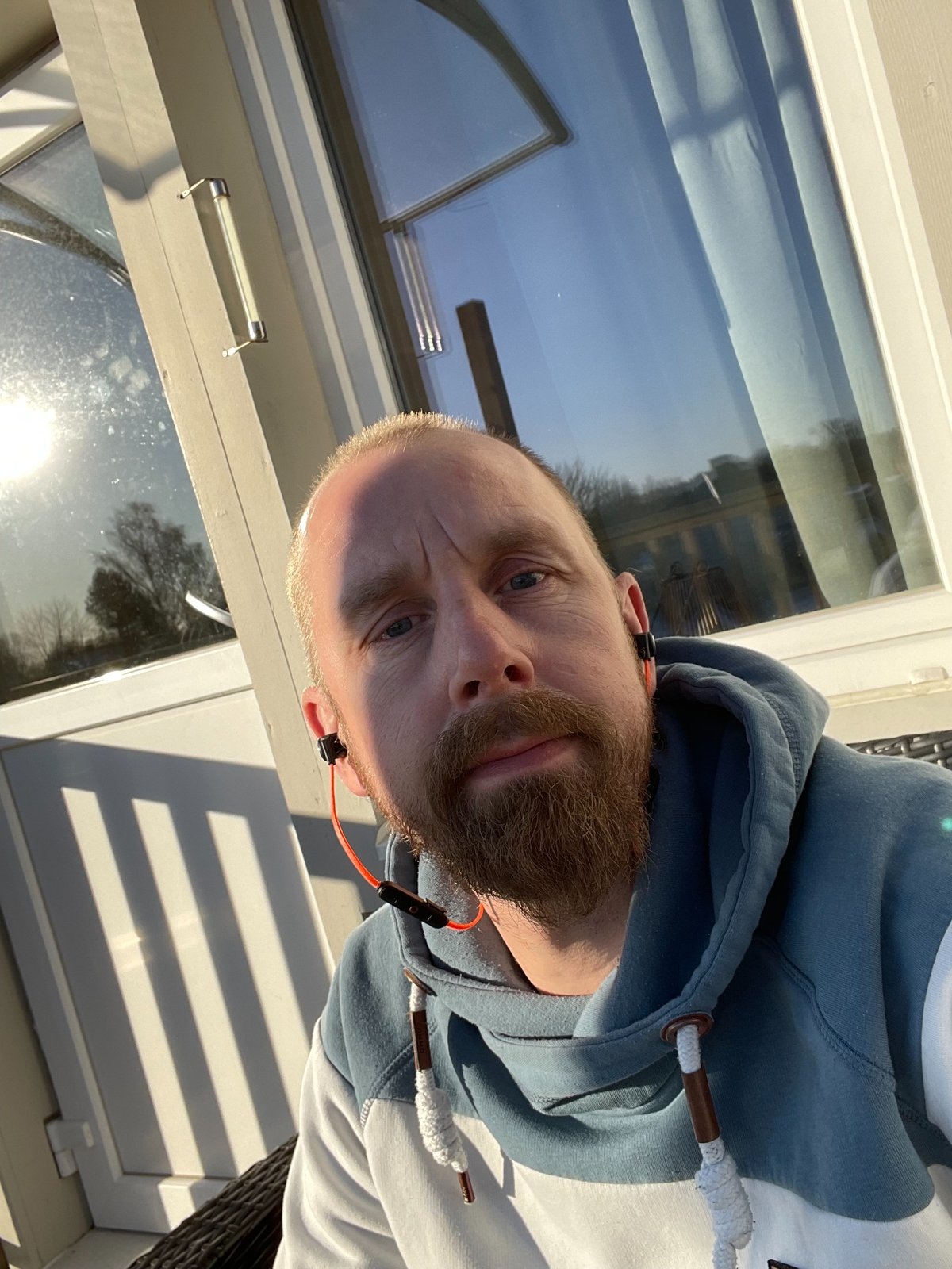 Man sitter utomhus i solen med hoodie och headset, ser avslappnad ut