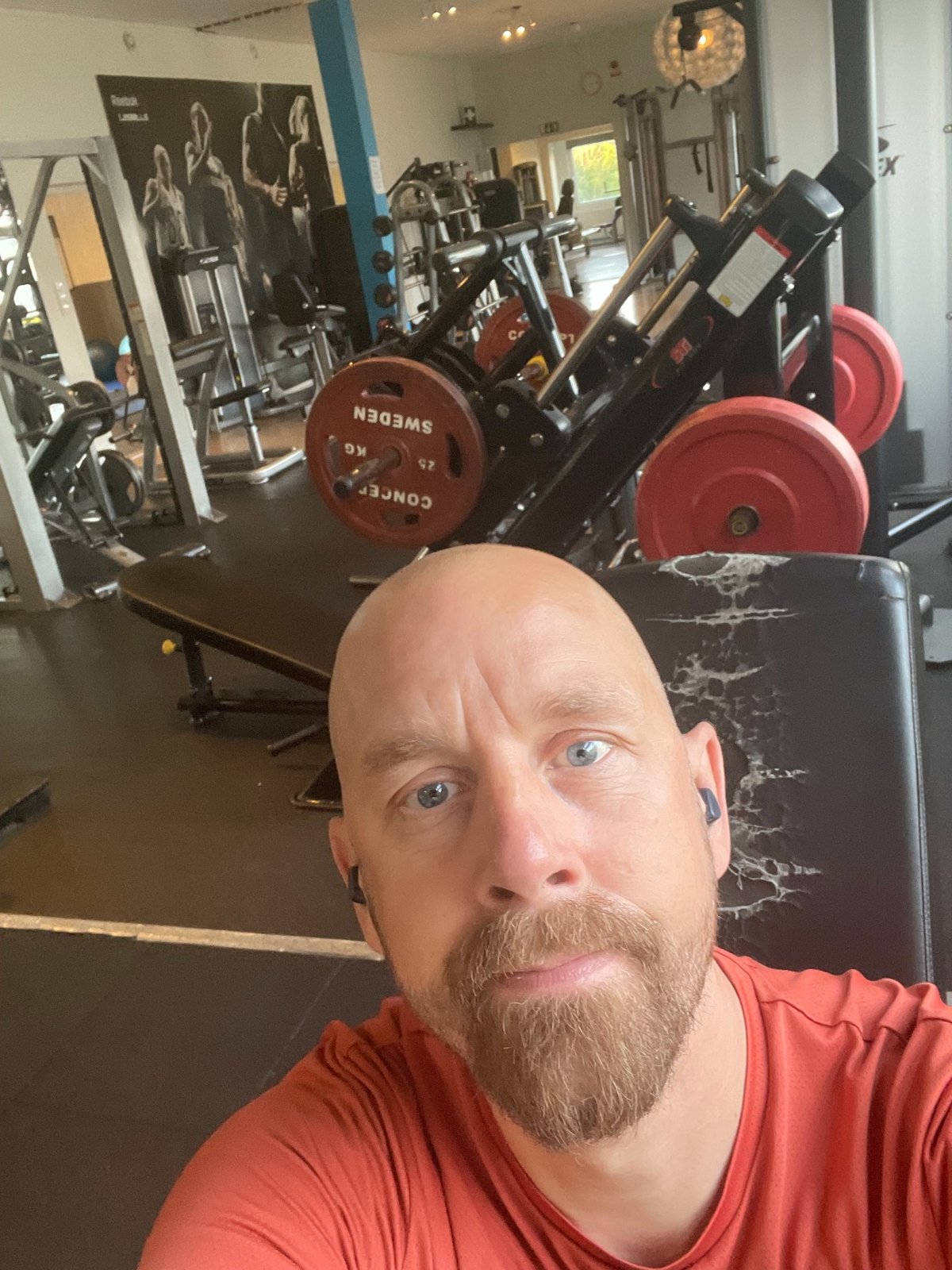 Personlig träningsselfie på gymmet med benpress i bakgrunden.