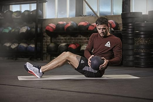 Person som sitter på en träningsmatta och håller en medicinboll för magträning med vridande rörelser