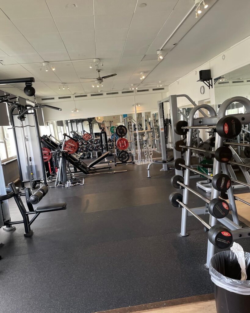 Gym med olika träningsmaskiner som latsdrag, sned benpress och skivstänger – komplett träningsutbud för styrketräning