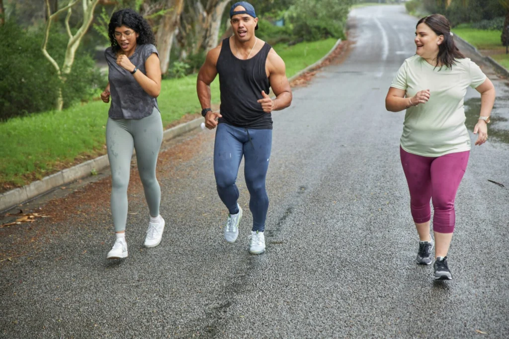 Tre personer joggar tillsammans i regnet, klädda i träningskläder, med fokus och energi.